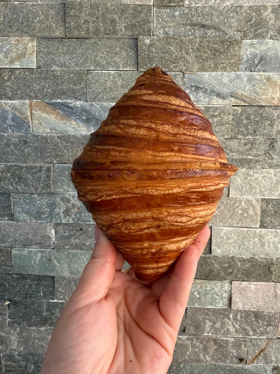Croissant dorado sostenido en una mano frente a una pared de piedra